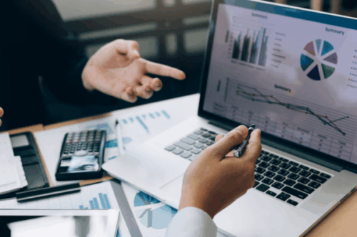 Two business professionals analyzing financial charts and graphs on a laptop during a meeting, illustrating How to Perform a Cash Flow Stress Test (Scenario Planning Templates Included).
