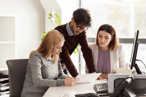 Three business professionals reviewing documents in a modern office, representing collaboration and planning, ideal for illustrating how tariff negotiations affect small business strategies.